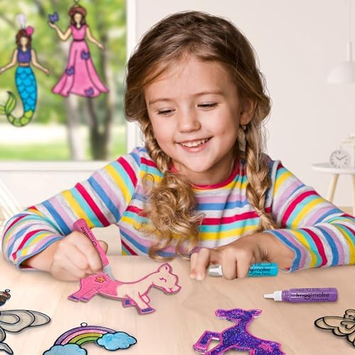 A young girl proudly holding her completed DIY glass painting suncatcher kit creations next to a window view.