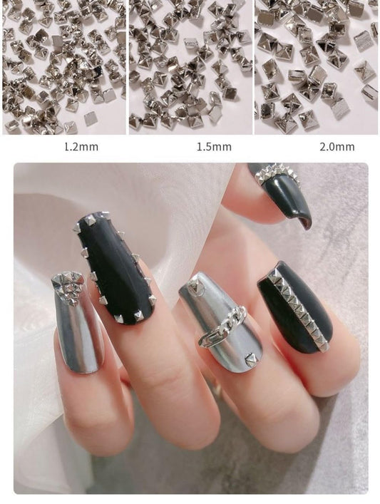 Close up view of miniature silver alloy spike charms for professional acrylic nail extensions.
