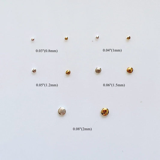 Close up view of miniature gold nail embellishments in various millimeter sizes on a flat surface.