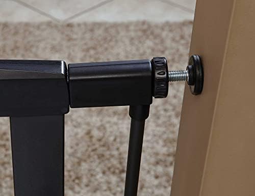 The nineteen inch wide door of the graphite metal dog gate swinging open in a spacious hallway setting.