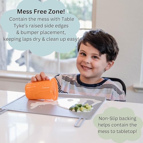 A toddler seated at a restaurant table using the Sage Green Table Tyke placemat to eat finger foods safely