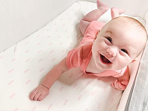 Geometric pink and white patterned baby changing table sheet displayed inside a modern nursery setting.