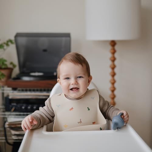 Premium Swedish design Mushie silicone bib in cream color with dinosaur print
