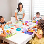 Hapinest reusable plastic placemats being wiped clean with a damp cloth on a dining table.