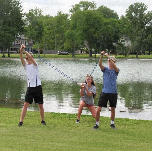 Three people setting up the giant backyard catapult toy to launch water balloons at an outdoor summer party.