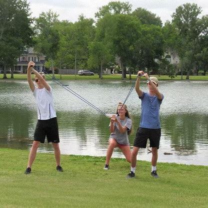 Three people setting up the giant backyard catapult toy to launch water balloons at an outdoor summer party.