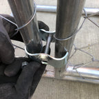 Close up view of a galvanized saddle style clamp wrapping around two parallel round metal pipes.