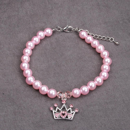 Small puppy wearing a pink pearl necklace with a sparkling rhinestone crown charm