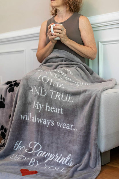 Pawprints Left by You gray plush fleece sympathy throw blanket displayed open on a sofa.