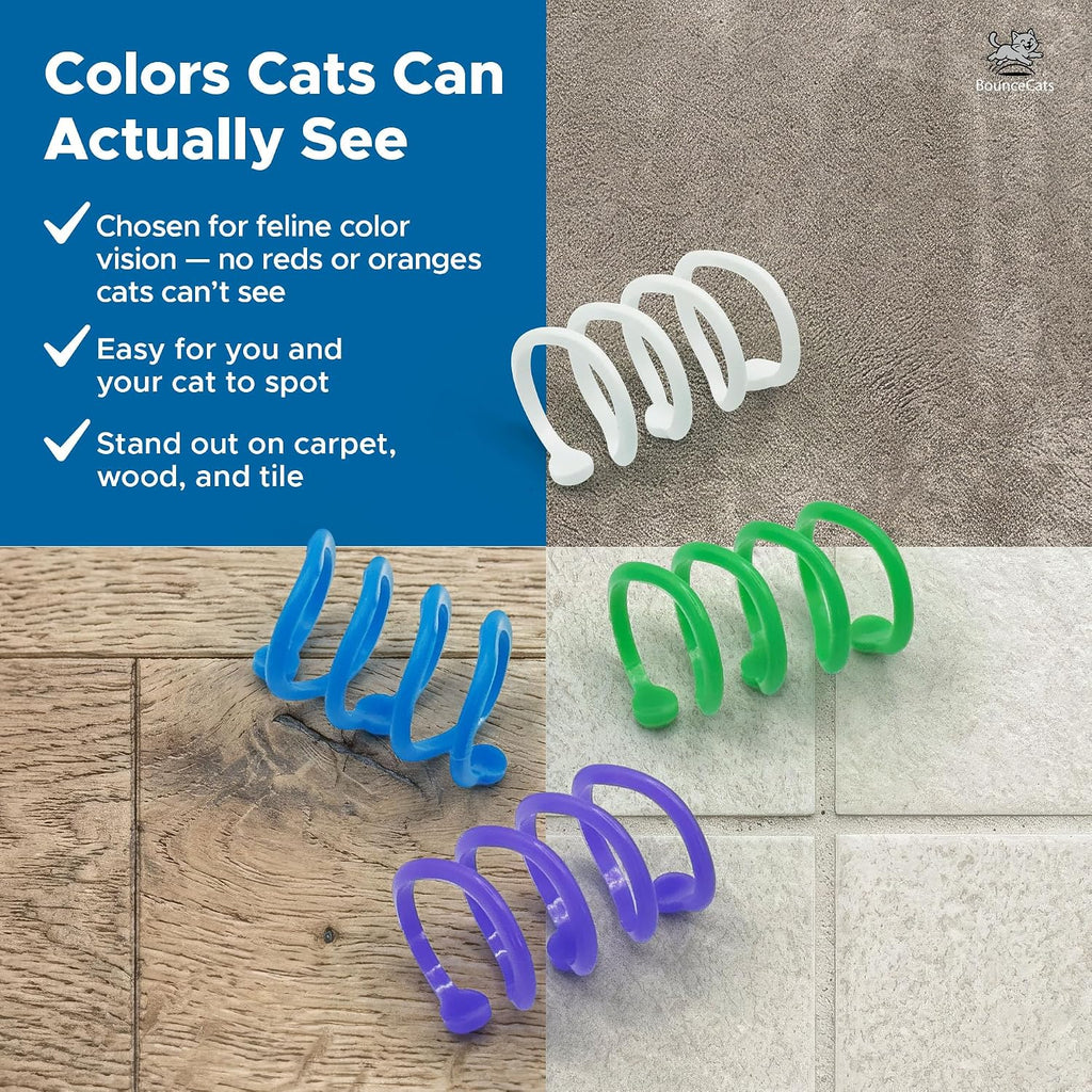 A playful kitten pouncing on a green BounceCats interactive spiral spring under a bright light.