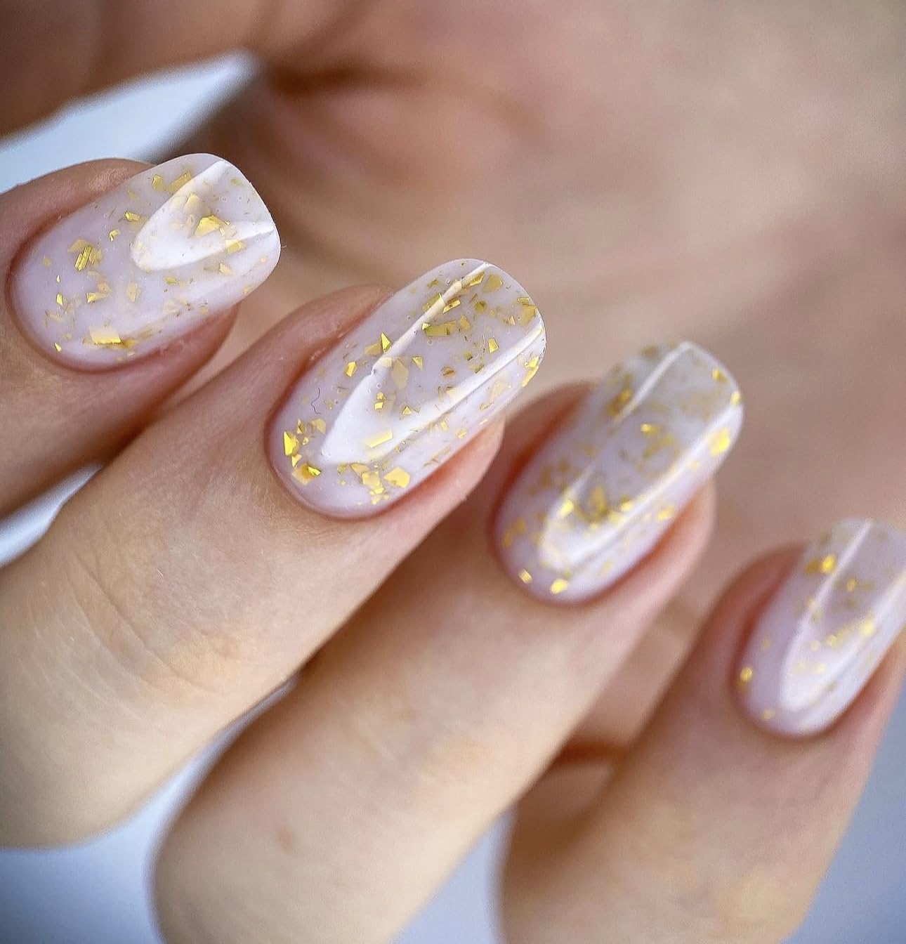 Close up of the semi sheer milky white gel polish texture showing delicate embedded gold flakes.