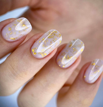 Close up of the semi sheer milky white gel polish texture showing delicate embedded gold flakes.