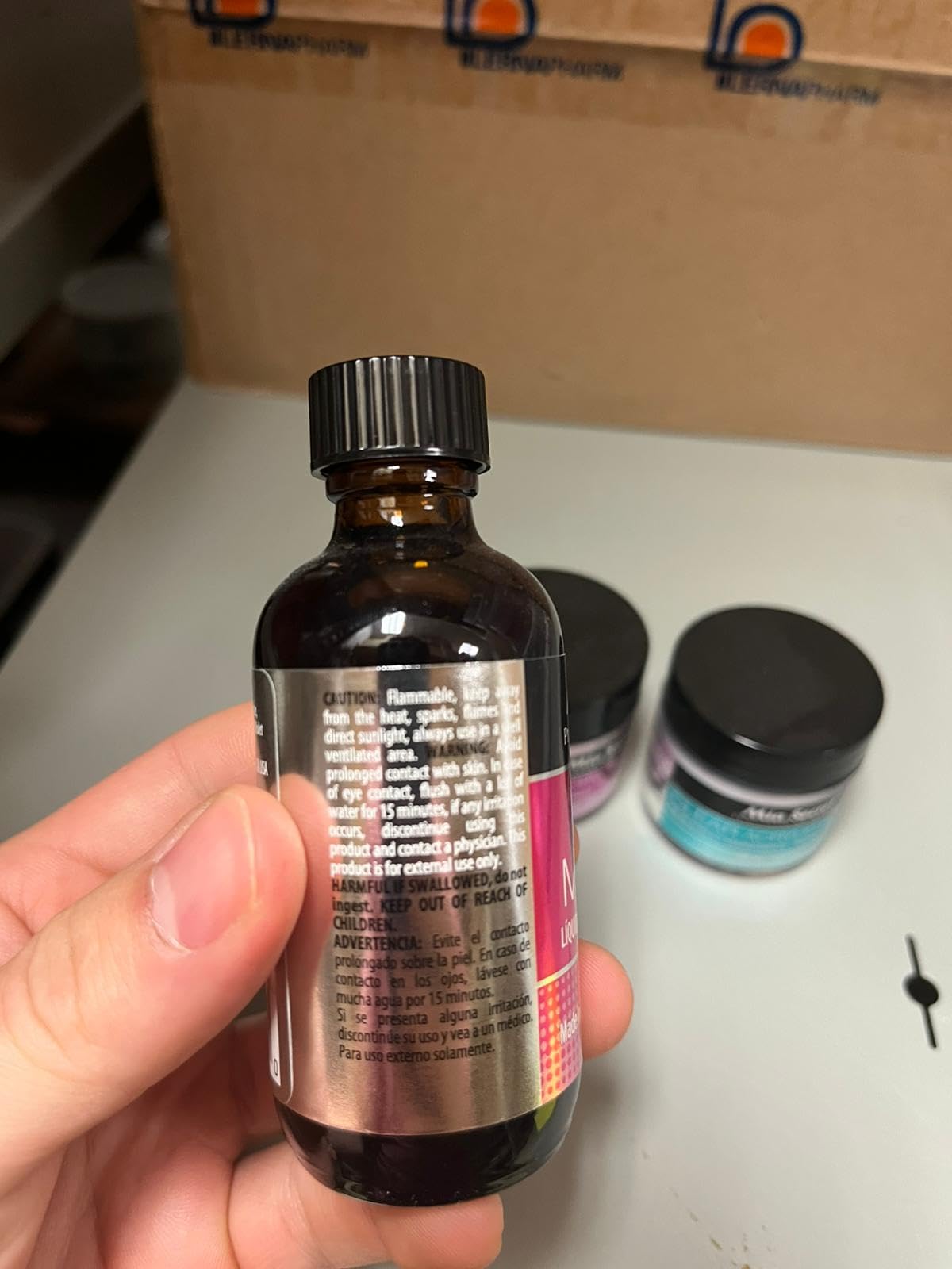 Two ounce liquid monomer fluid bottle beside one ounce pink polymer powder jar