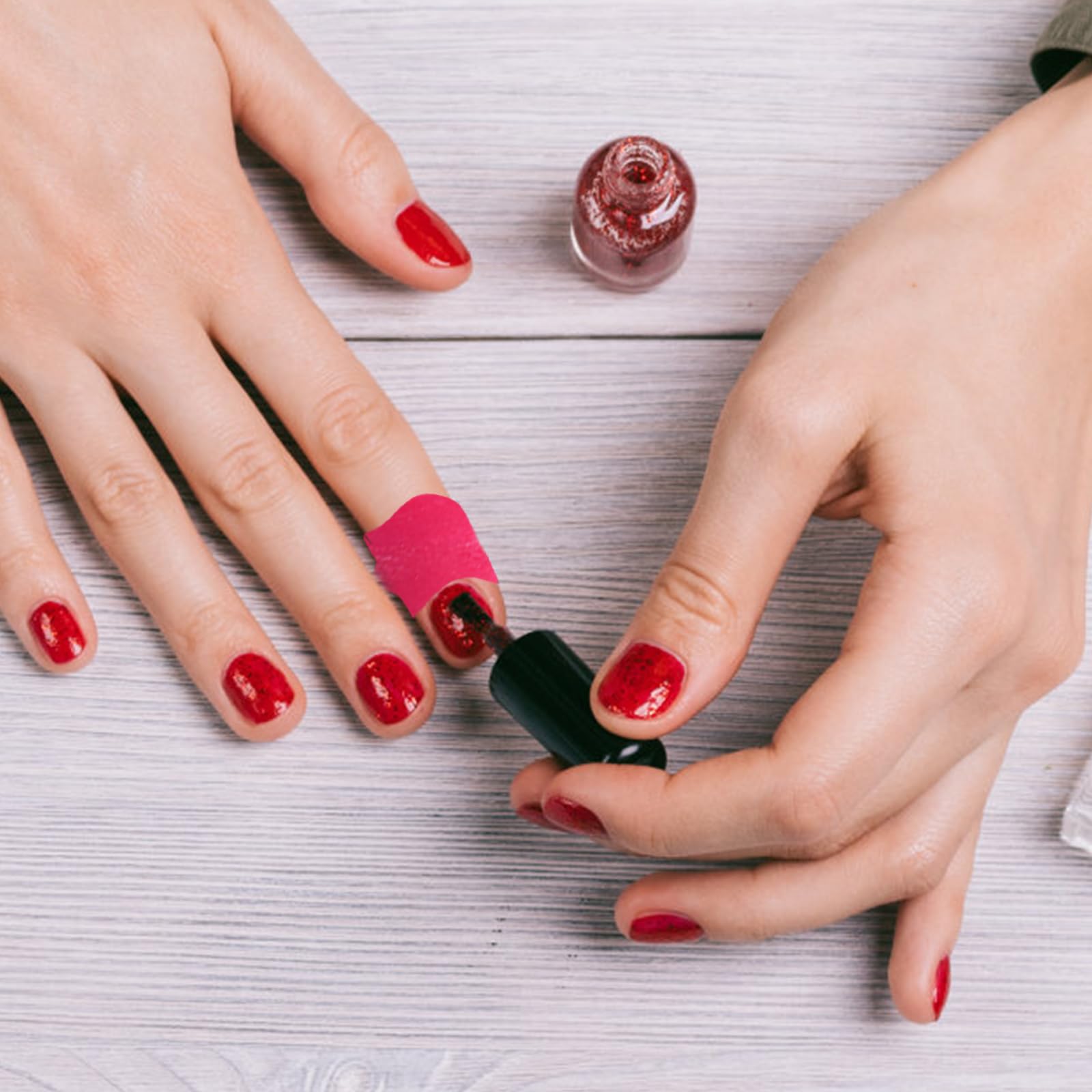 Close-up of a hand applying a pink Oruola U-shape latex barrier around the cuticle for mess-free nail art painting.