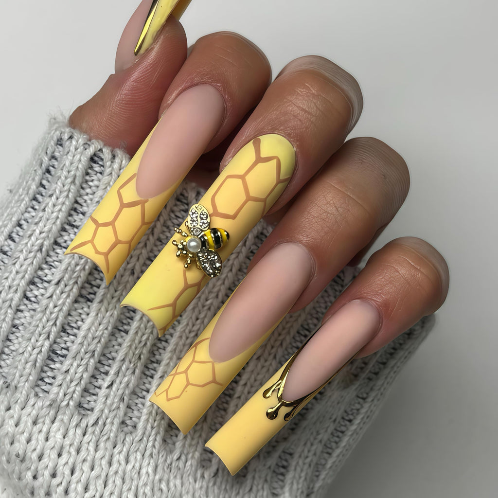Finished manicure showcasing applied gold bee and daisy charms.