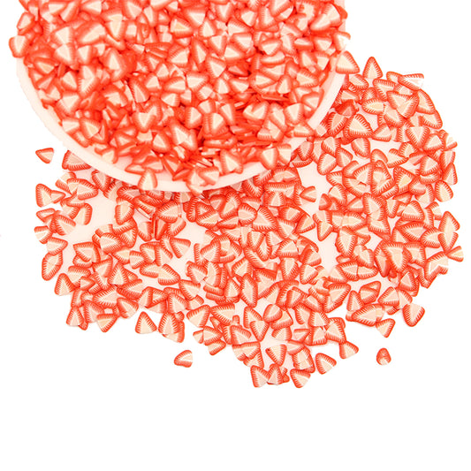 Close up view of red and white three dimensional polymer clay strawberry charms used for DIY slime decoration.