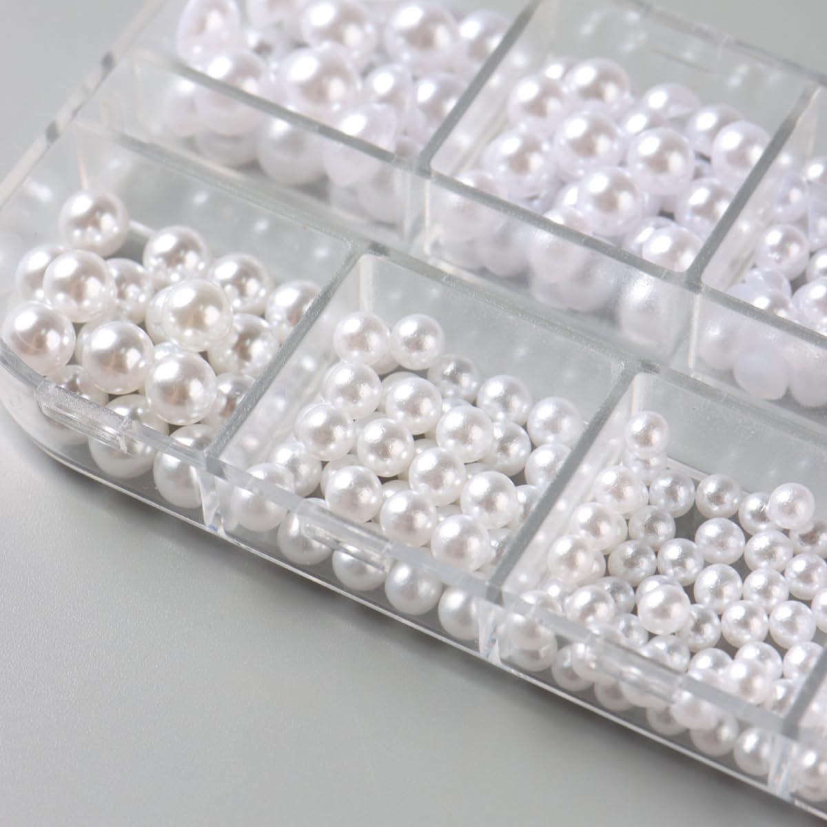 Various sizes of white nail pearls displayed on a surface