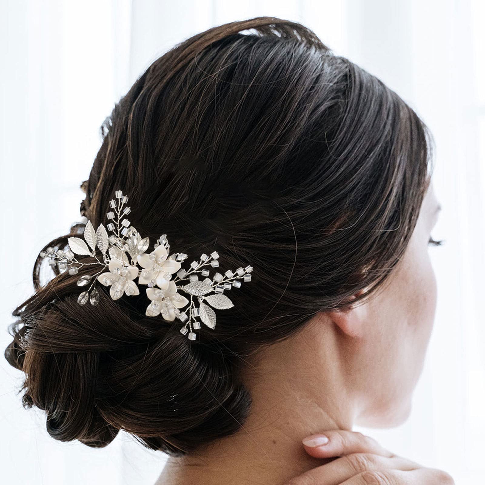 Handmade silver bridal hair piece showing detailed white ceramic flowers and sparkling rhinestones.