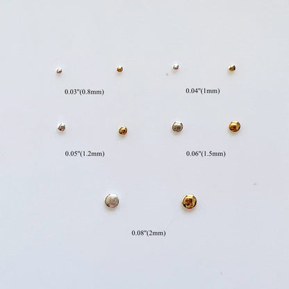 Close up view of miniature gold nail embellishments in various millimeter sizes on a flat surface.