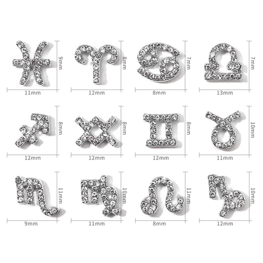 Close up view of gold and silver alloy zodiac nail charms showing embedded rhinestones and detailed constellation words.