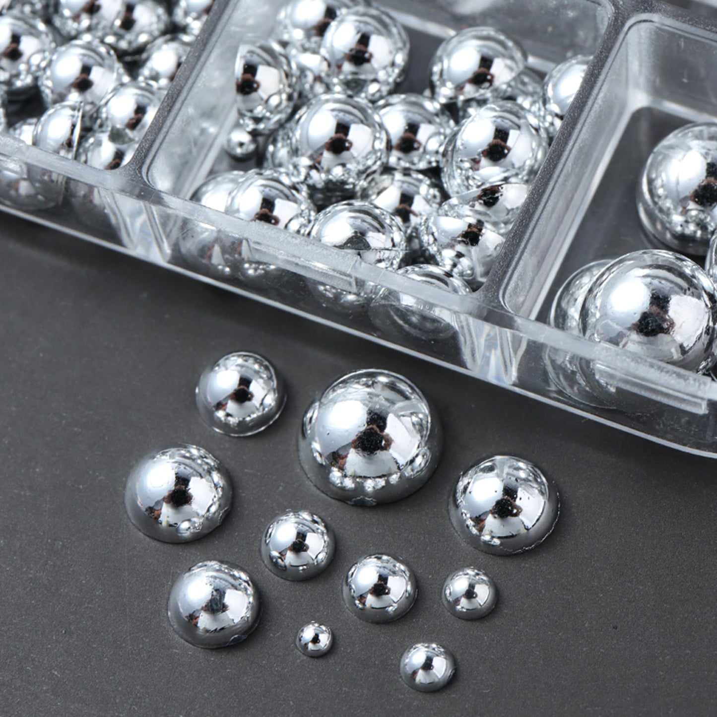 Two clear storage boxes filled with mini metal rivet punk nail charms alongside application tweezers