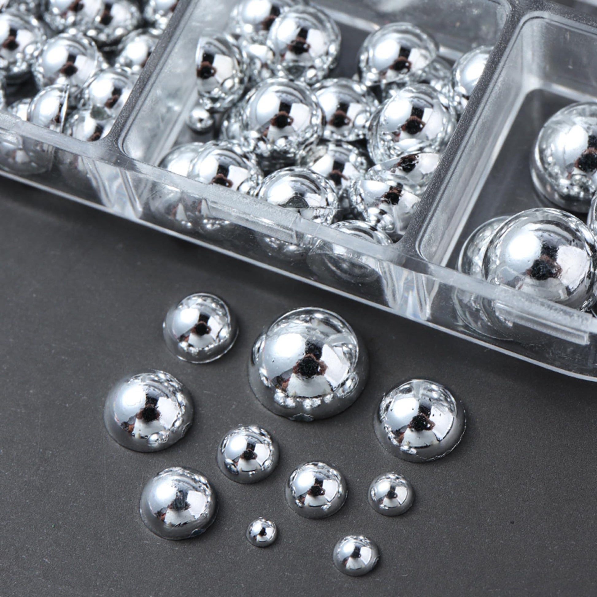 Two clear storage boxes filled with mini metal rivet punk nail charms alongside application tweezers
