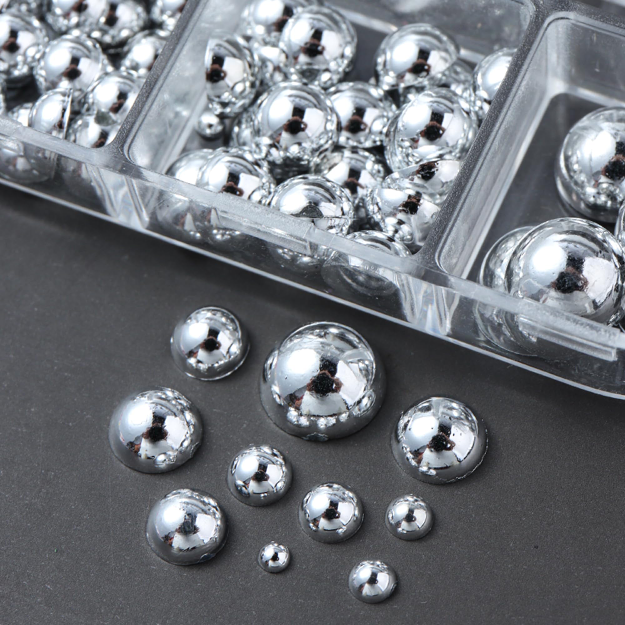 Two clear storage boxes filled with mini metal rivet punk nail charms alongside application tweezers