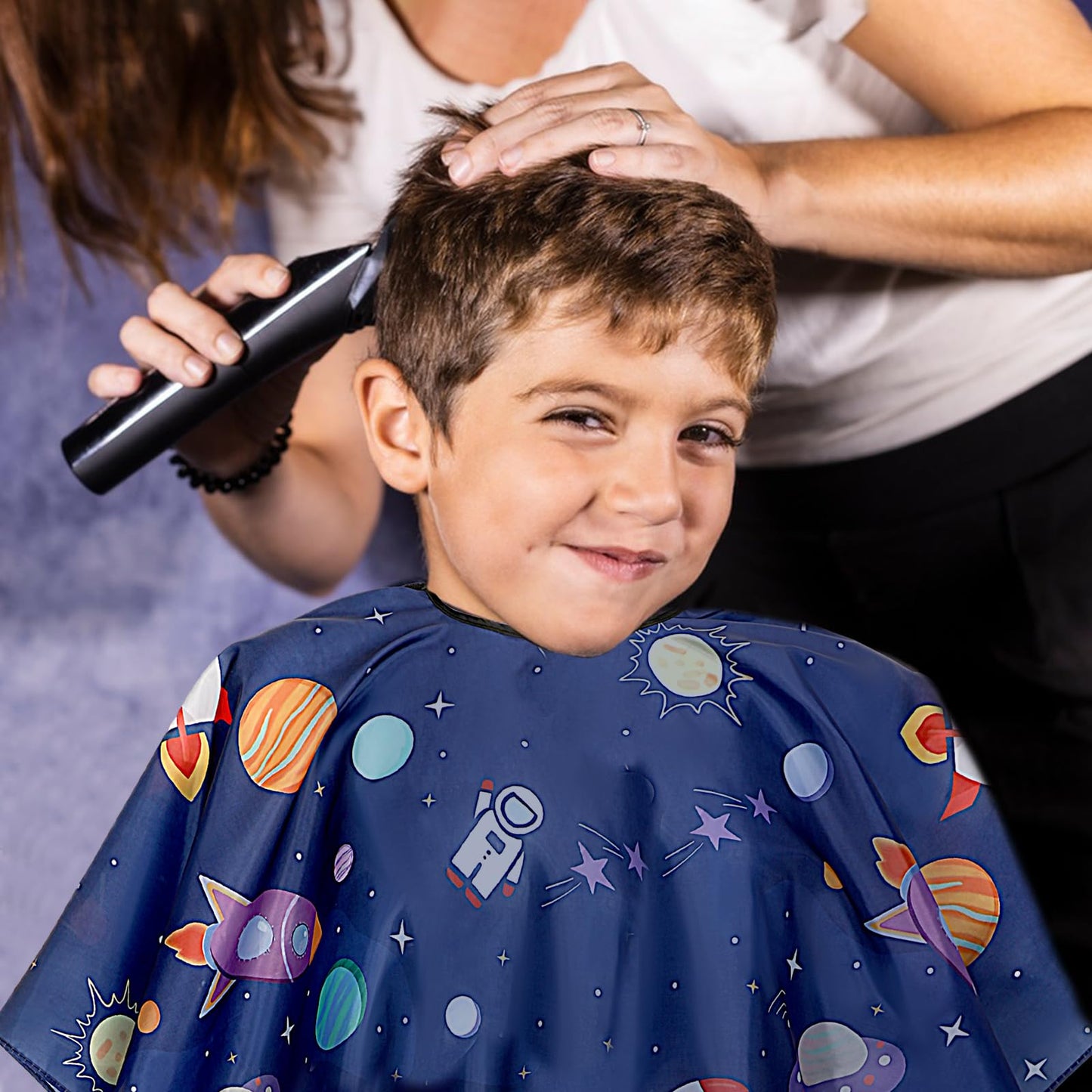 Child sitting comfortably in salon chair with hair cutting cape