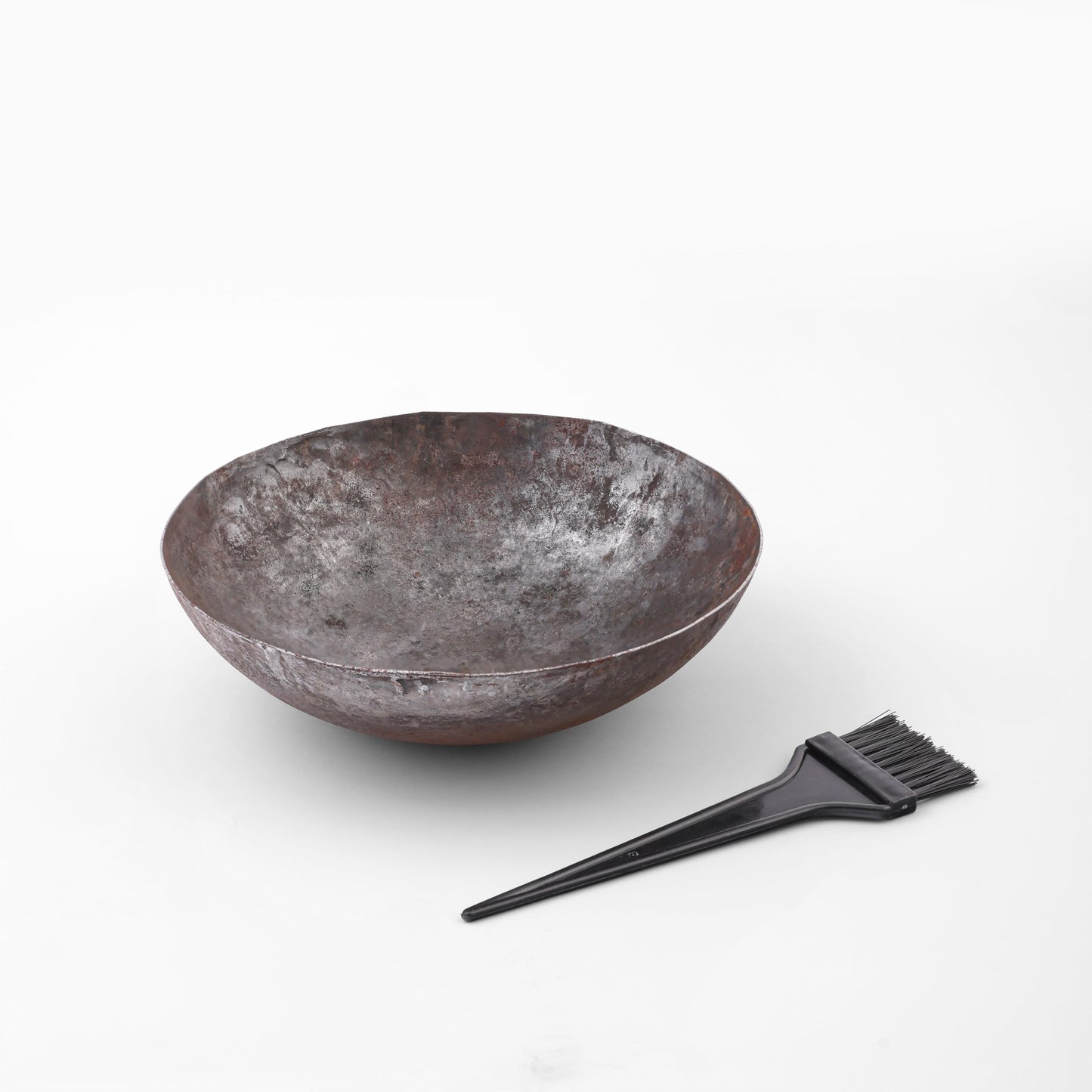 Black plastic hair dye brush resting on pure solid iron bowl