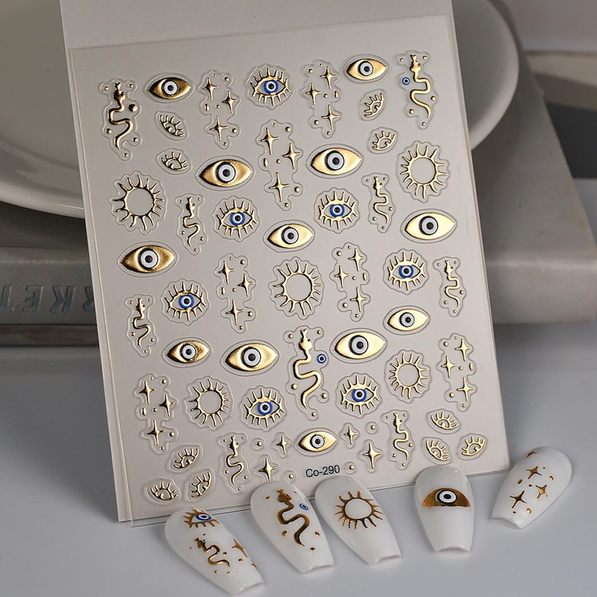 Applying gold evil eye nail stickers with tweezers