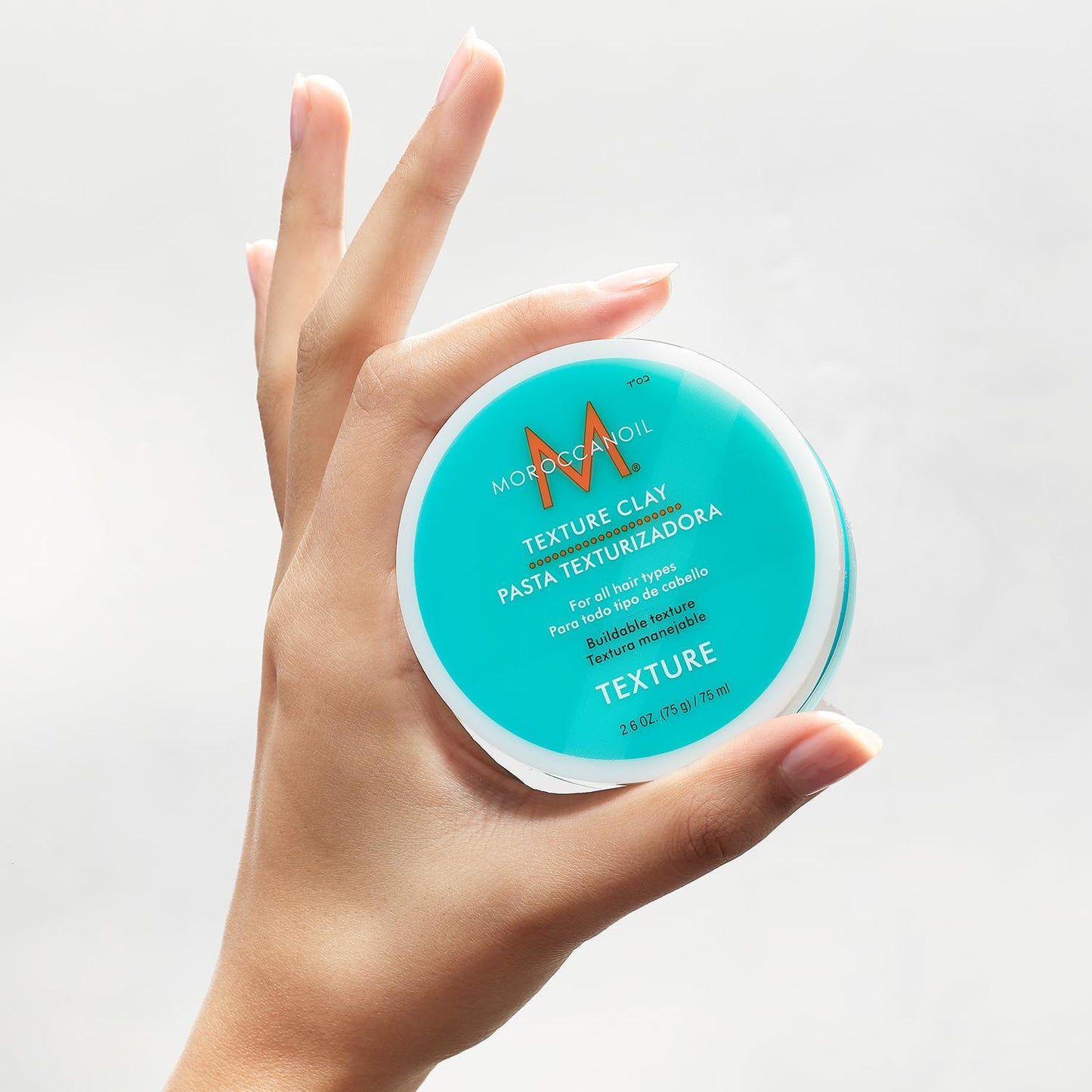 Open jar of Moroccanoil hair styling clay displaying its creamy bentonite texture.