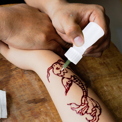 Demonstration of the flexible henna bottle being squeezed for precise freehand mehndi and body paint application.