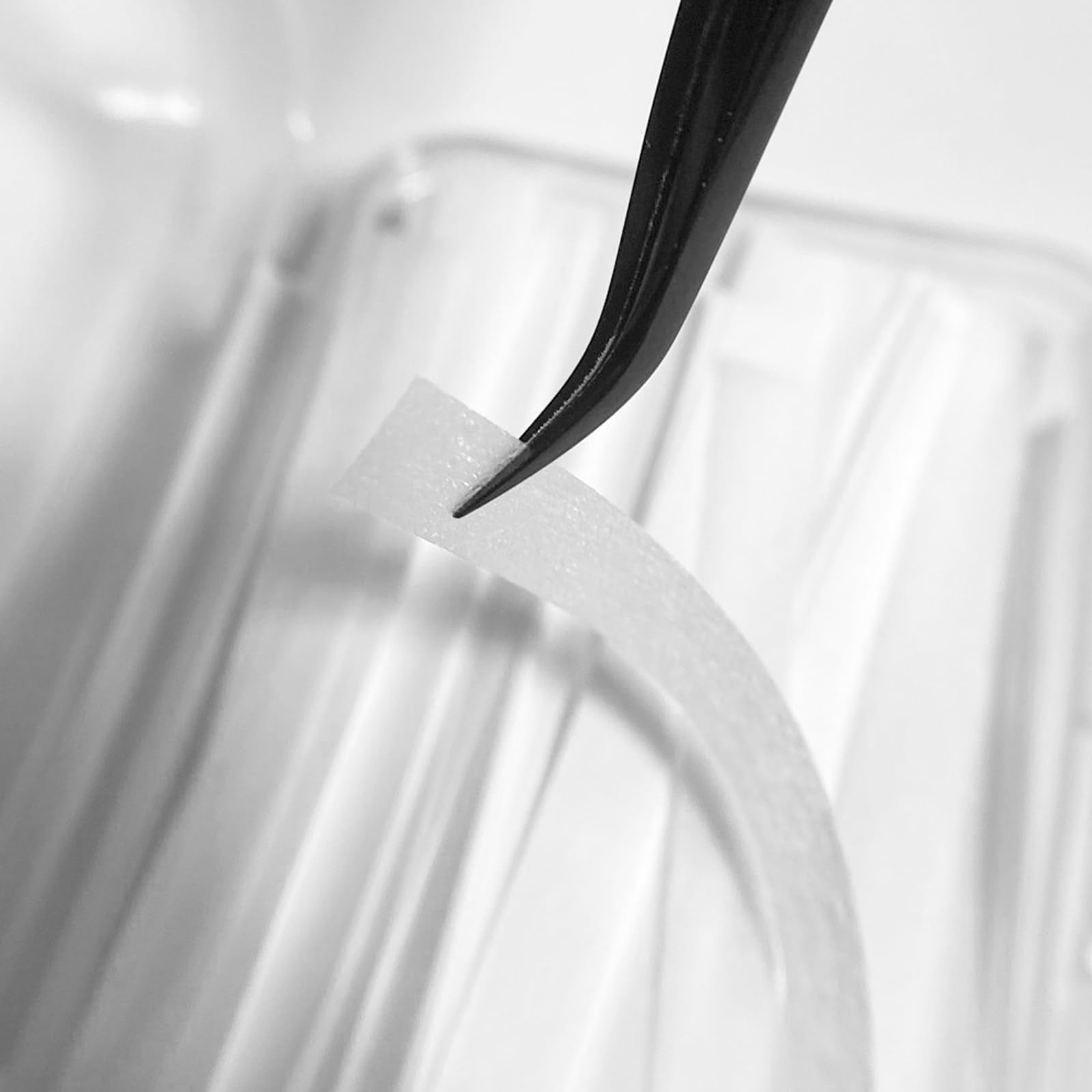 A professional lash artist applying the white PERMANIA ribbon tool over client eyelashes during a perming session.