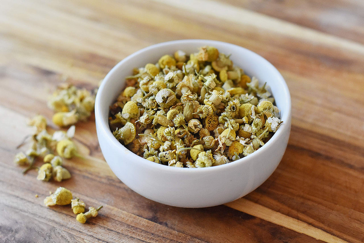 Freshly brewed golden chamomile tea in a clear glass cup alongside the premium whole loose leaf flowers.