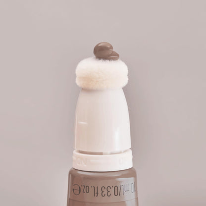A lifestyle shot of the authentic imported Essence liquid bronzer placed with other clean beauty products.