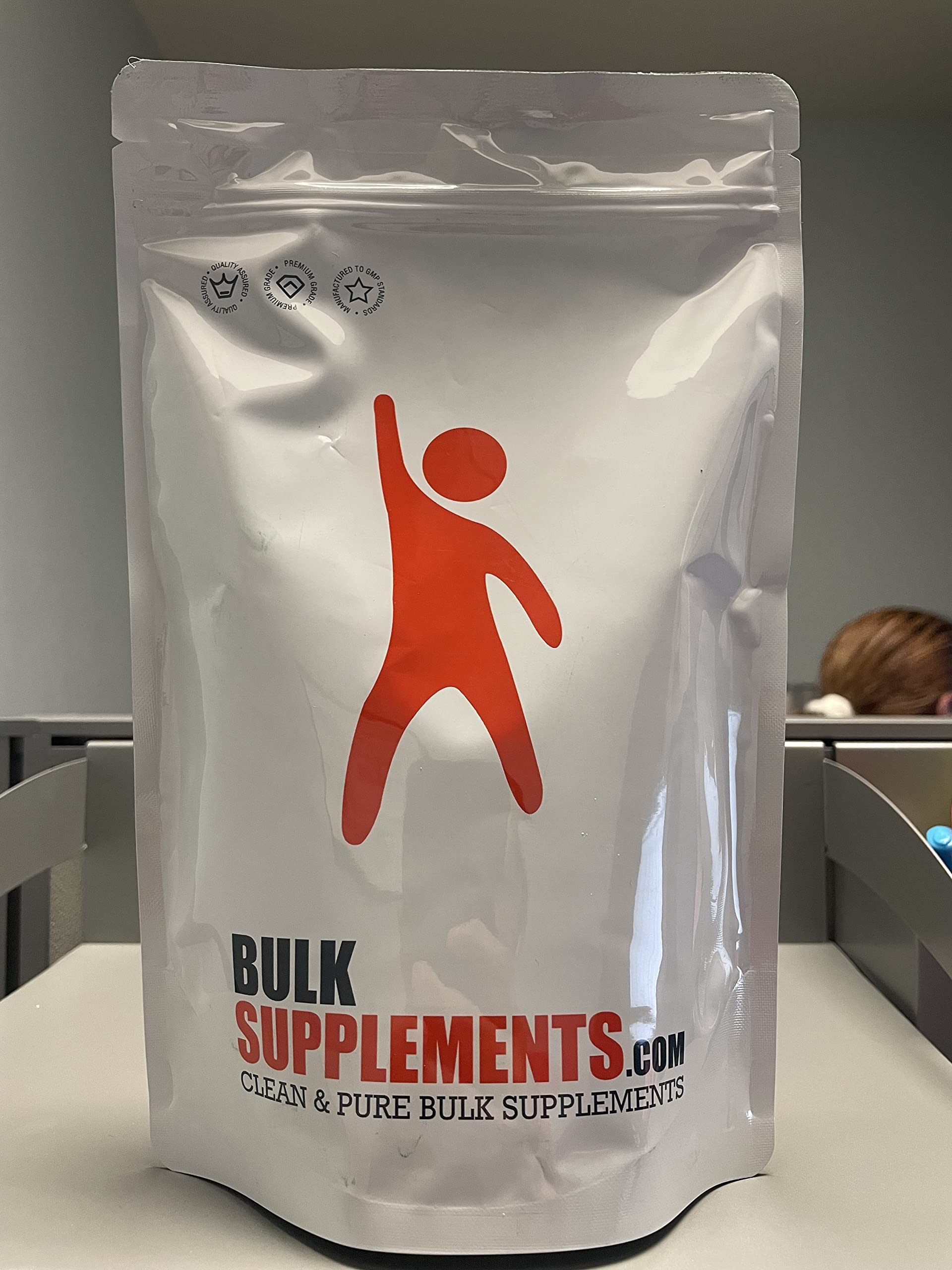 Pure green spirulina powder from BulkSupplements poured next to its authentic imported packaging.