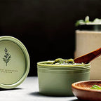 Self-heating wash-off mask jar next to its protective box container on a clean surface.