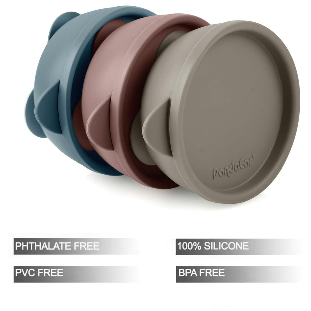 Three silicone toddler suction bowls with spill-proof lids arranged on a table