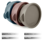Three silicone toddler suction bowls with spill-proof lids arranged on a table