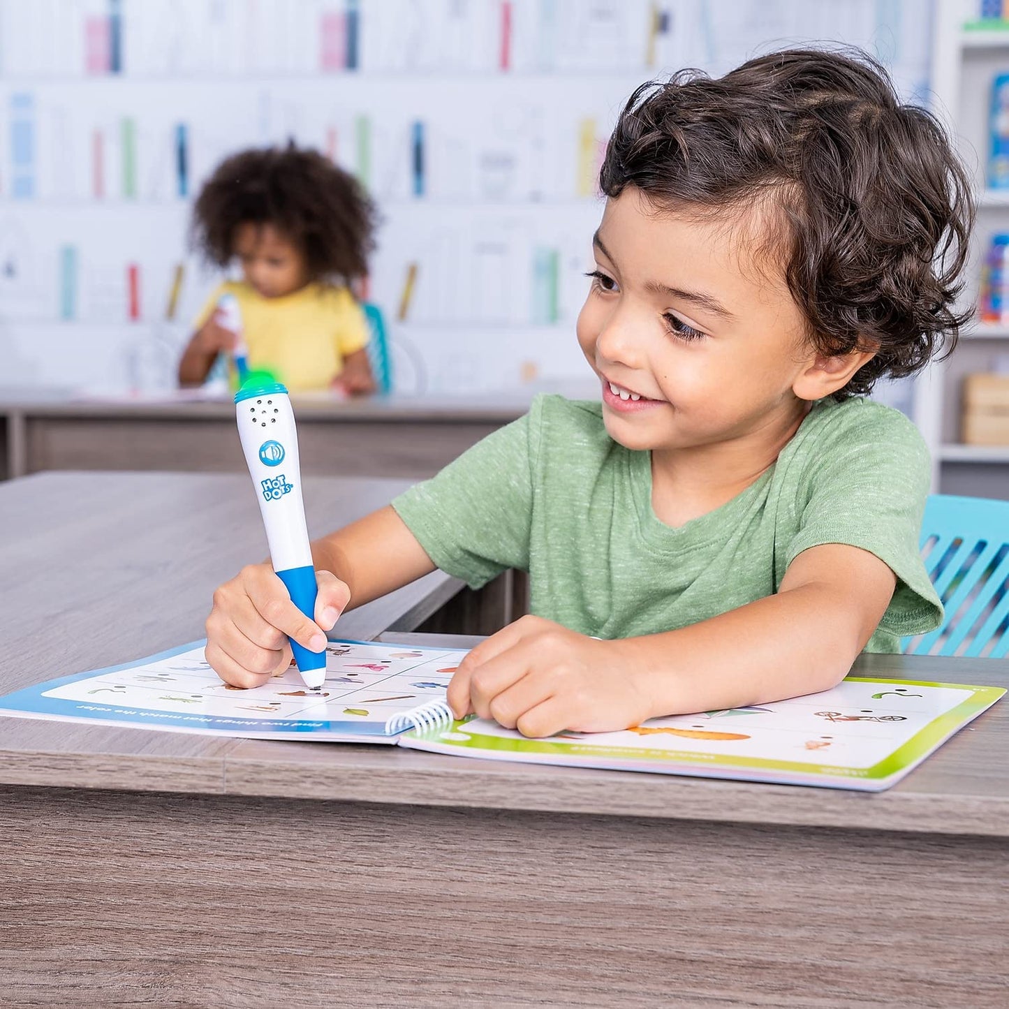 Preschool child using the green light-up interactive pen on the Hot Dots activity book pages