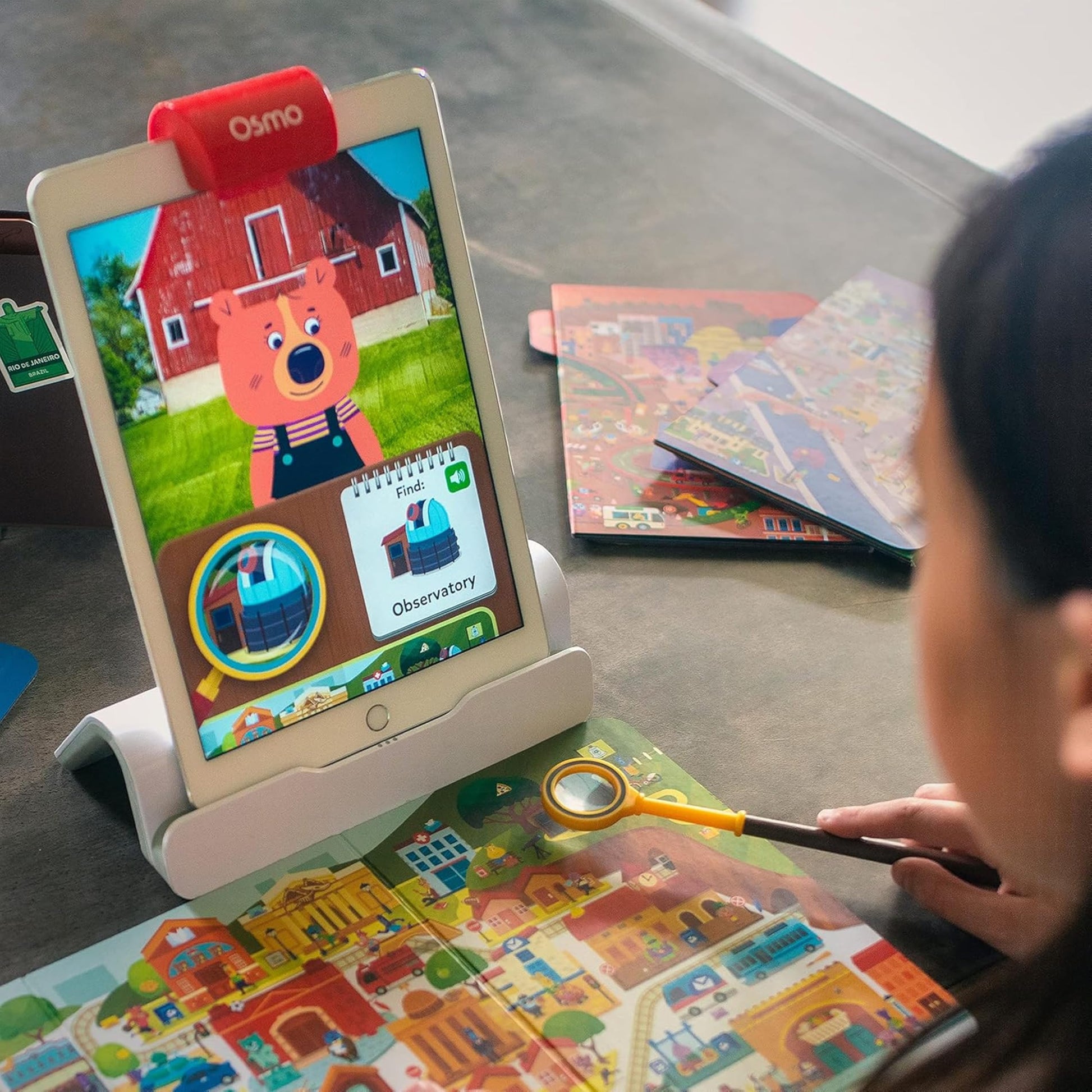 Child using the physical magnifying glass over detailed world maps for interactive tablet play
