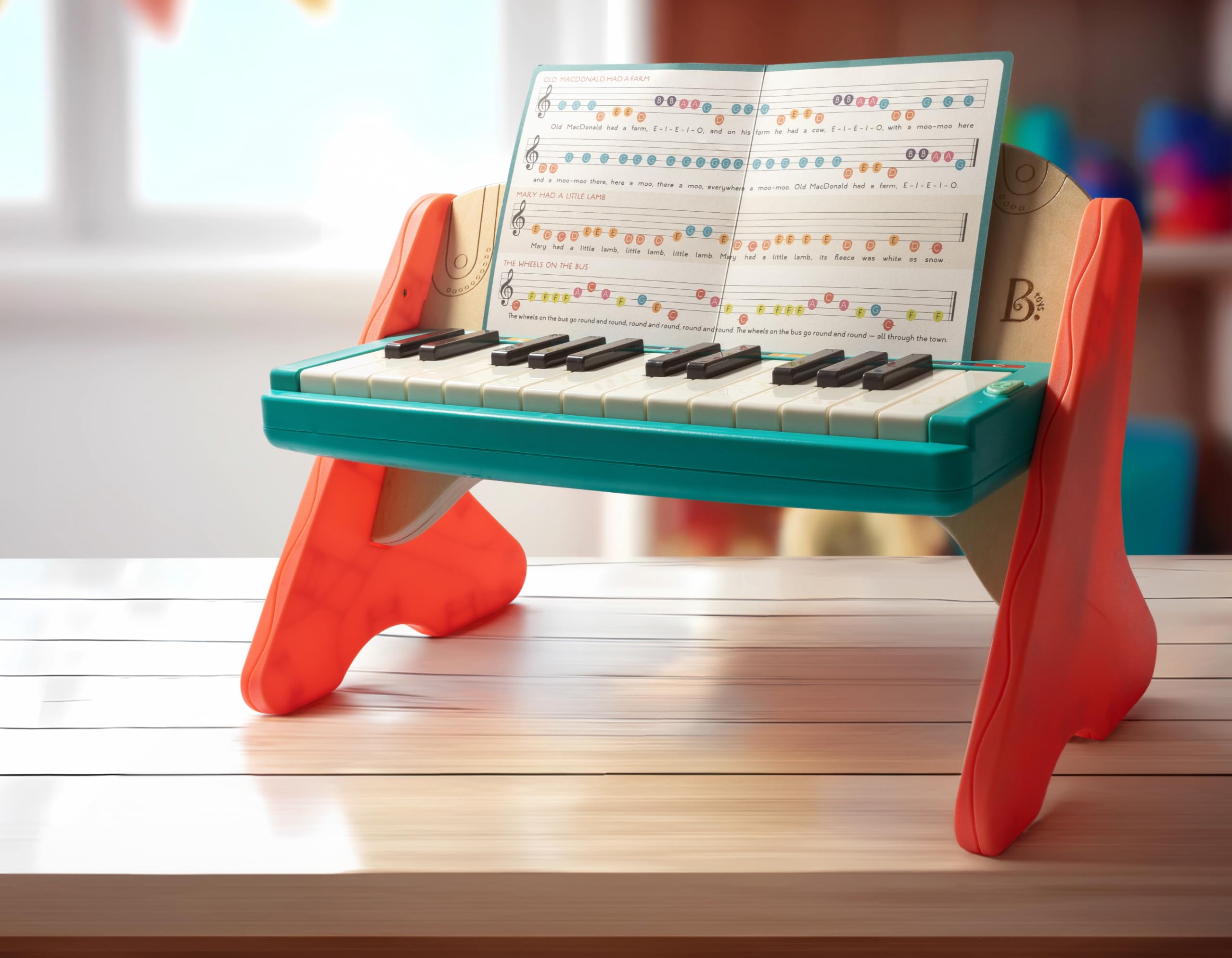 B. toys Mini Maestro wooden toddler piano with the included illustrated melody sheet book on the stand