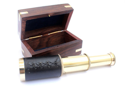 Vintage nautical brass telescope standing upright next to its closed anchor wooden storage case