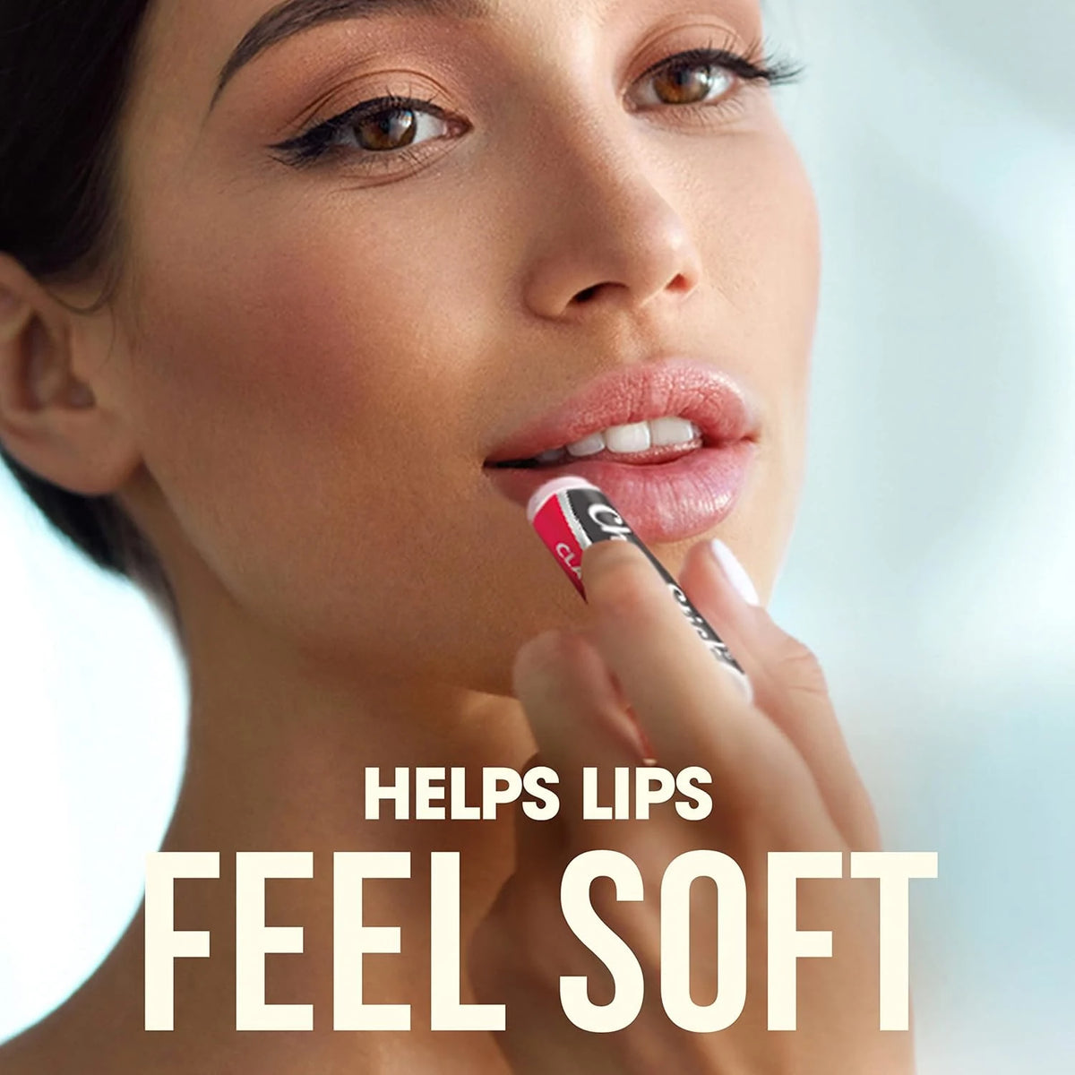 Woman applying lipstick with text 'HELPS LIPS FEEL SOFT' on a blurred background